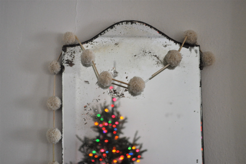 a christmasy garland the straw and pompom garland hanging on a mirror
